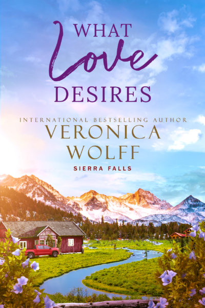 Book cover for What Love Desires by Veronica Wolff, Sierra Falls series, showing a red farmhouse and red pickup truck beside a winding creek below snowcapped mountains, framed by purple flowers.